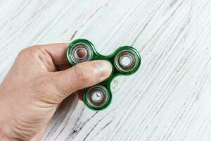 boy hand playing with fidget spinner gadget. Green hand spinner, fidgeting hand toy rotating on man hand photo