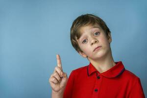 A cute Caucasian boy of 5 years old in a red T-shirt thoughtfully, seriously and edifiingly points his finger up photo