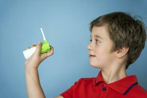 A cute 5-year-old Caucasian boy in a red T-shirt holds in his hand a can of aerosol for the treatment of sore throat photo