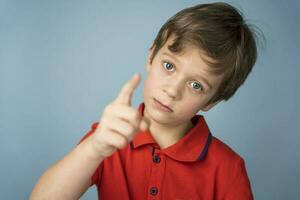 A cute Caucasian boy of 5 years old in a red T-shirt thoughtfully, seriously and edifiingly shakes his finger photo