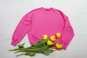 Closeup pink blank template sweatshirt hoodie copy space. Mothers women day yellow tulips, gifts. Happy birthday top view mockup pullover. White wooden background. Casual outfit. Flat lay templates photo