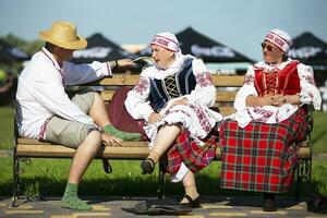 08 29 2020 Belarus, Lyaskovichi. Celebration in the city. People in national Slavic clothes are sitting on the bench. Belarusians or ukran man and women. photo