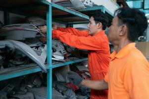 Two mechanics are selecting automobile parts, car headlights, from a spare parts warehouse in order to replace a collision's damaged headlights photo