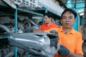 Two mechanics are selecting automobile parts, car headlights, from a spare parts warehouse in order to replace a collision's damaged headlights photo