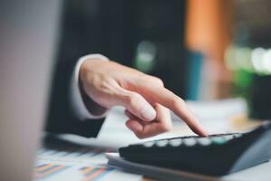 Businessman using a calculator to calculate numbers ,profit and loss statement review of company performance, cost analysis ,financial paperwork ,account checking ,chart analysis and statistical data photo