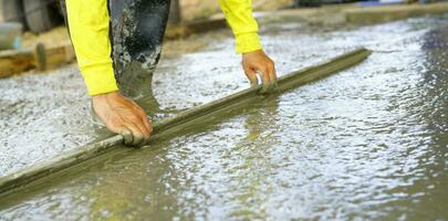 Construction worker leveling wet concrete floor with a trowel at construction site. Construction worker working with ready-mix concrete. Construction contractor concept. Builder slab cement after pour photo