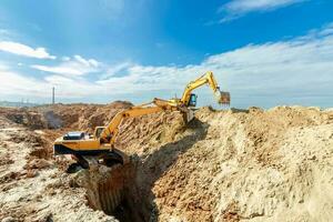 dos excavador son excavación suelo en el construcción sitio en cielo fondo, con blanco mullido nube foto