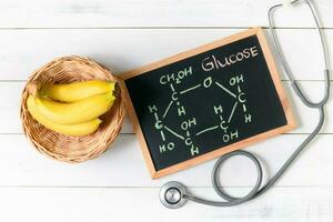 Glucose molecule on blackboard with banana and stethoscope photo