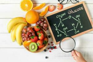 Glucose molecule on blackboard with mixed fresh fruits salad photo