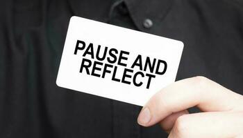 Businessman holding a card with text PAUSE AND REFLECT, business concept photo