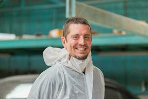 alegre trabajador hombre en un reparar cochera, mecánico pintura coche en pie en cámara, garaje pintura coche Servicio reparar y mantenimiento foto