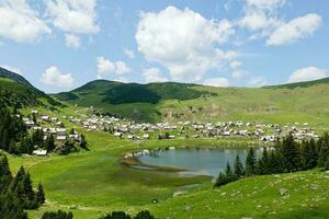 escénico punto de vista terminado prokosko lago en bosnia y herzegovina soleado día con nubes rural vida y tradicional vida. glacial lago. vranica montañas en el antecedentes. rústico chozas foto