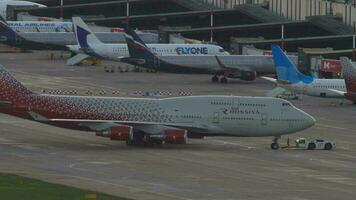 SOCHI, RUSSIA JULY 28, 2022 - Tractor pullsing aircraft Rossiya on the runway at Sochi airport. Boeing 747 on the apron. Row of planes docked at the terminal. Tourism and travel concept video