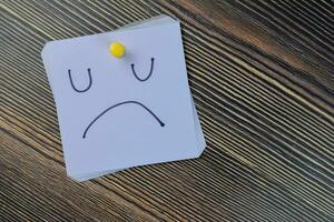 Concept of Unhappy booring moody emotion face write on sticky notes isolated on Wooden Table. photo