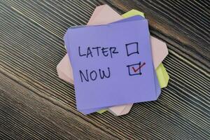 Concept of do it now or later write on sticky notes isolated on Wooden Table. photo