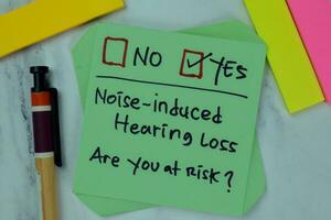 Concept of Noise-Induced Hearing Loss, are you at risk write on sticky notes isolated on Wooden Table. photo