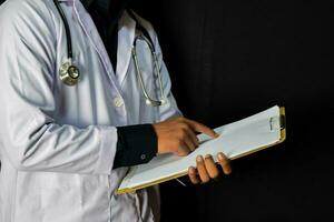 doctor standing holding clipboard on black background. Medical and healthcare concept photo