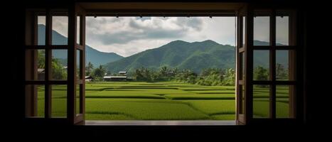 A window view of a rice field with mountains in the background. photo