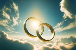 A pair of gold wedding rings floating in the sky. two wedding rings floating in the clouds with a sun in the background and a blue sky with clouds below them. . Wedding concept. photo