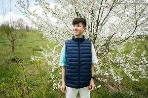 Teen boy wear sleeveless vest against white blloming tree in spring. photo