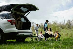 Mother with children sit on chair against car open trunk on picnic. photo