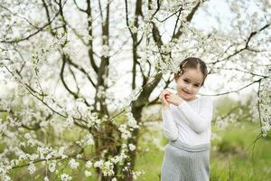 Portrait of preschool girl against white blloming tree in spring. photo