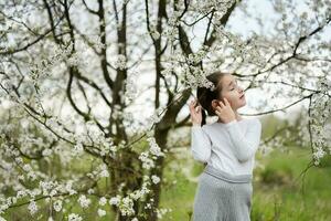 retrato de preescolar niña en contra blanco floreciente árbol en primavera. foto