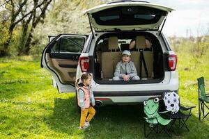 Brother with sister sit on car open trunk at picnic. photo