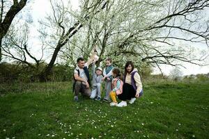 Family with three kids in spring meadow on the background of a flowering tree. photo