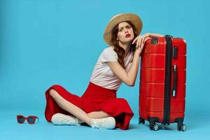 cheerful woman in hat sitting on the floor red suitcase passenger isolated background photo