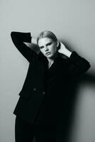 A striking blonde girl in a classic suit holds her hair with her hands and poses like a professional model in a studio in black and white style. Fashion photography. Concept for clothing stores photo