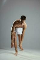 atleta con un mejorado torso en blanco pantalones cortos en un gris antecedentes inclinado adelante adentro foto