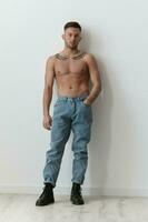 Sporty Sexy Muscular Handsome Naked Man holds hand on jeans looks at camera posing isolated on over white studio background. Cool fashion offer. Model shoot for ad. Copy space. Full body portrait photo