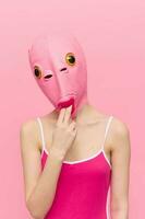 Funny woman in a sexy costume with a pink fish mask on her head put her fingers in her mouth in pink clothes on a pink background. The concept of modern art photography photo