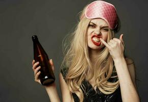 enojado mujer con un botella de cerveza en su mano con brillante maquillaje y un rosado dormir máscara foto