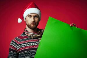 Cheerful man in a santa hat holding a banner holiday red background photo