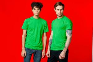 two friends in green t-shirts communication red background studio photo