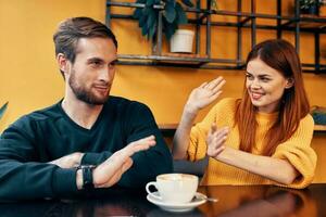 alegre hombre y mujer gesticulando con su manos y sentado a un mesa en un café comunicación amigos un taza de café foto