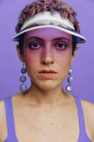 Portrait of a sporty fashion woman posing in a purple sports suit for yoga and a transparent cap on a purple background monochrome photo