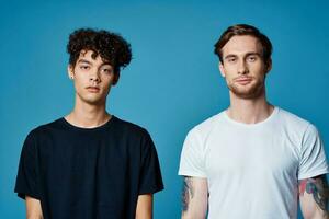 curly guy in a black t-shirt and a man with a tattoo on a blue background friends chatting photo