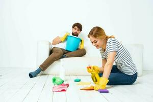 A man sits on a sofa with a bucket of a woman on the floor with a detergent for kitchen interior chores photo