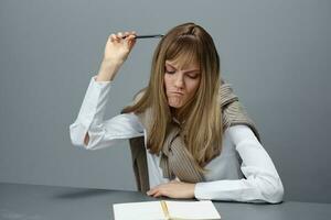 Pensive young blonde student lady freelancer in warm sweater scratching head with pen have no idea for essay in gray modern home office. Remote Job, Education And Career Profession Concept. Copy space photo