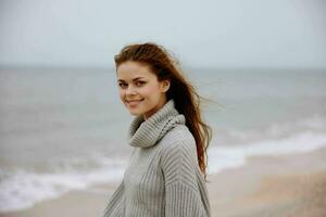 cheerful woman in a sweater flying hair by the ocean tourism Happy female relaxing photo