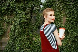 alegre mujer con corto pelo al aire libre un taza con un bebida verano vacaciones foto