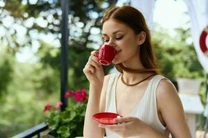 joven elegante mujer en un blanco vestir bebidas café al aire libre en un café verano día foto