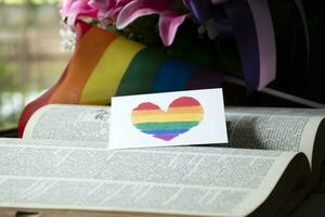 Closeup view of bookmark in heart shape which drew with rainbow colours, blurred opened old book background, concept for calling out all people to respect gender diversity of humans in pride month. photo