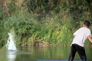 Asian boy in white t-shirt is spending his freetimes by diving, swimming, throwing rocks and catching fish in the river happily, hobby and happiness of children concept, in motion. photo