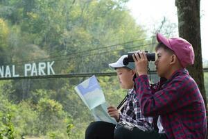 Asian boys holding binoculars and national map and reading map details about bird watching and fish watching by the river bank in local national park, nature study and environment learning concept. photo