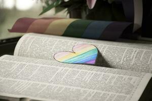 Closeup view of bookmark in heart shape which drew with rainbow colours, blurred opened old book background, concept for calling out all people to respect gender diversity of humans in pride month. photo