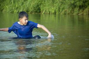 Asian boy in blue t-shirt is spending his freetimes by diving, swimming, throwing rocks and catching fish in the river happily, hobby and happiness of children concept, in motion. photo